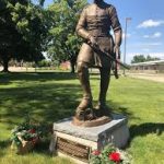 General John ONeill Statue Nebraska Directory Bronze statue of a uniformed soldier standing with a rifle in a park on a stone pedestal with flowers at the base