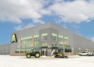 AKRS Oneill Nebraska Directory Modern industrial showroom building with green trimmed glass facade a green tractor and a yellow skid steer sit at the entrance area
