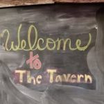 The Tavern Nebraska Directory Chalkboard sign reading Welcome to The Tavern in yellow and pink letters with a rustic chalkboard backdrop
