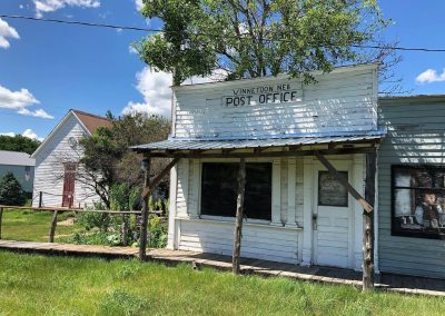 Old white wooden post office in Winnetoon Nebraska with a porch blue sky and surrounding greenery
