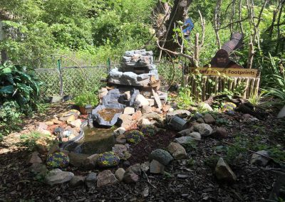 Fantasy Forest Footprints Garden Nebraska Directory Whimsical garden display with a small waterfall and sign reading Fantasy Forest Footprints