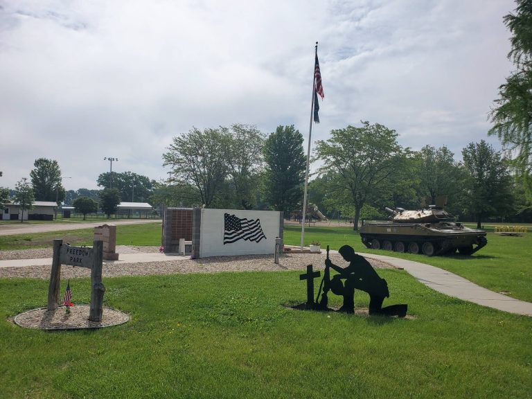 Veterans memorial at Freedom Park in Battle Creek with flag walls, a kneeling soldier silhouette and the U.S. flag
