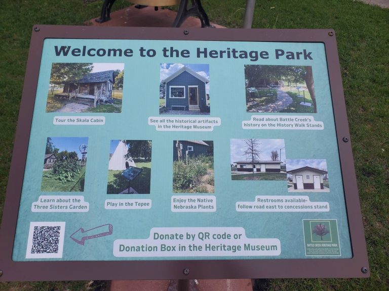Welcome sign at Battle Creek Heritage Park showing the Skala cabin, Heritage Museum, History Walk, Three Sisters Garden and tepee